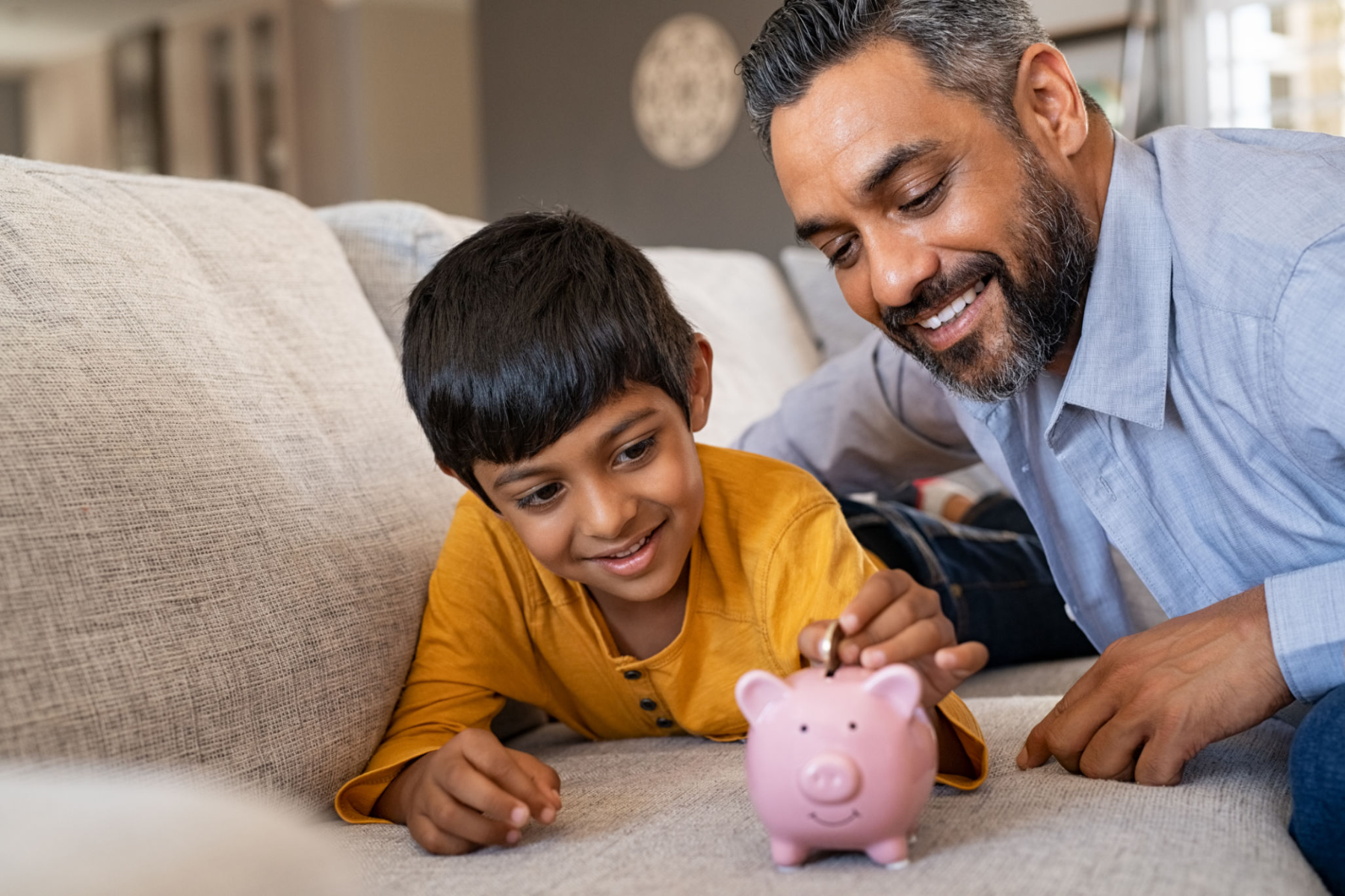 Indian son and father putting coins in piggy bank